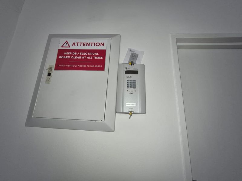 A utility wall section featuring a mounted electrical distribution board with safety signage and an integrated alarm system keypad.