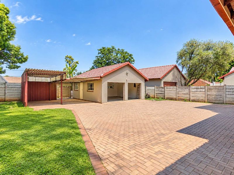 Spacious rear exterior featuring a double garage, attached carport, extensive paved driveway, and well-maintained lawn enclosed by precast walling.