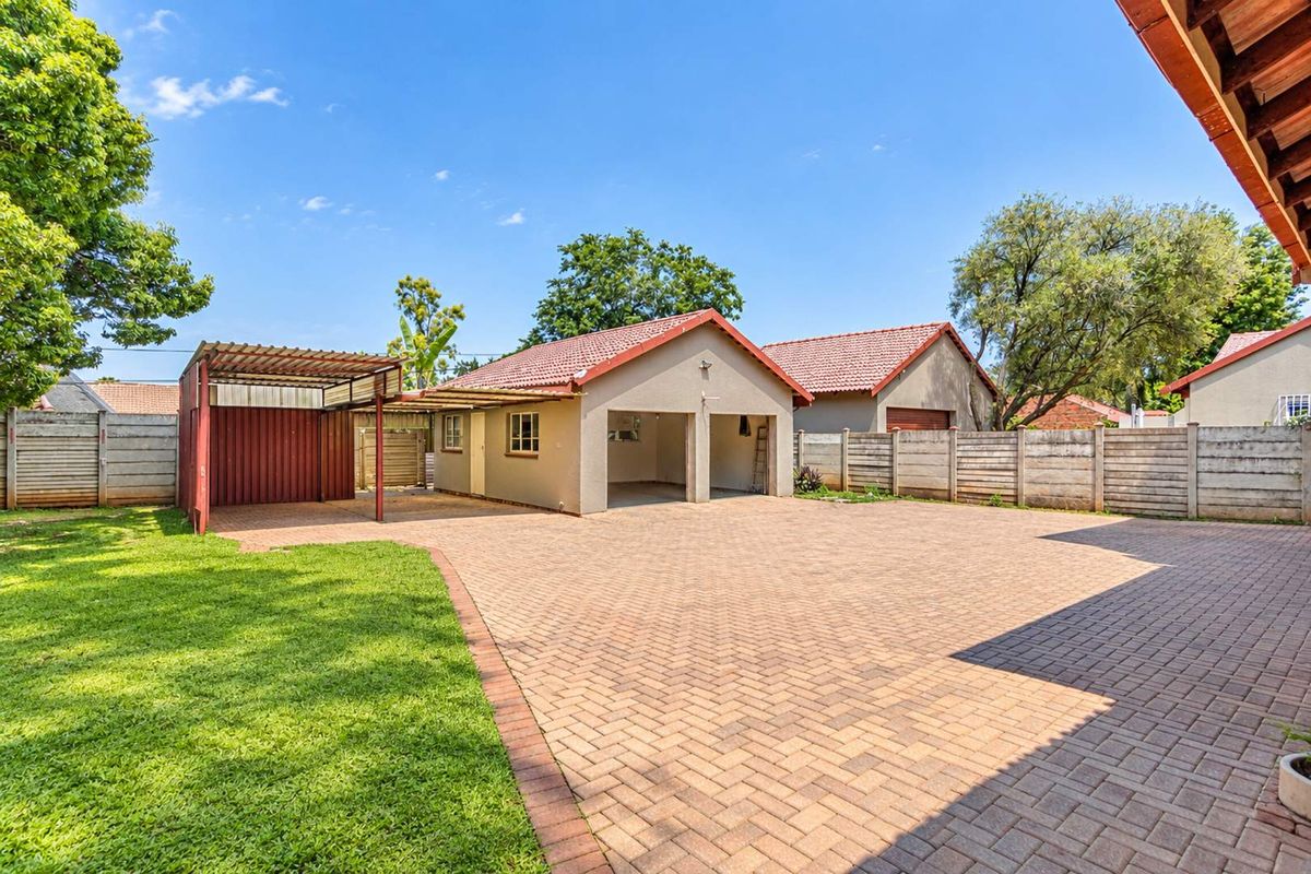 Spacious rear exterior featuring a double garage, attached carport, extensive paved driveway, and well-maintained lawn enclosed by precast walling.