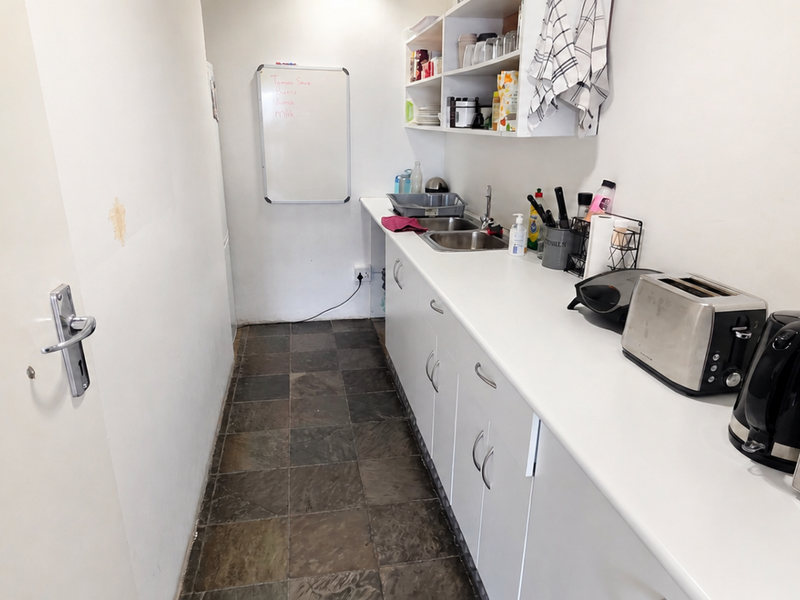 A functional scullery or kitchenette area featuring built-in cabinetry, open shelving, a stainless steel sink, and durable tiled flooring.