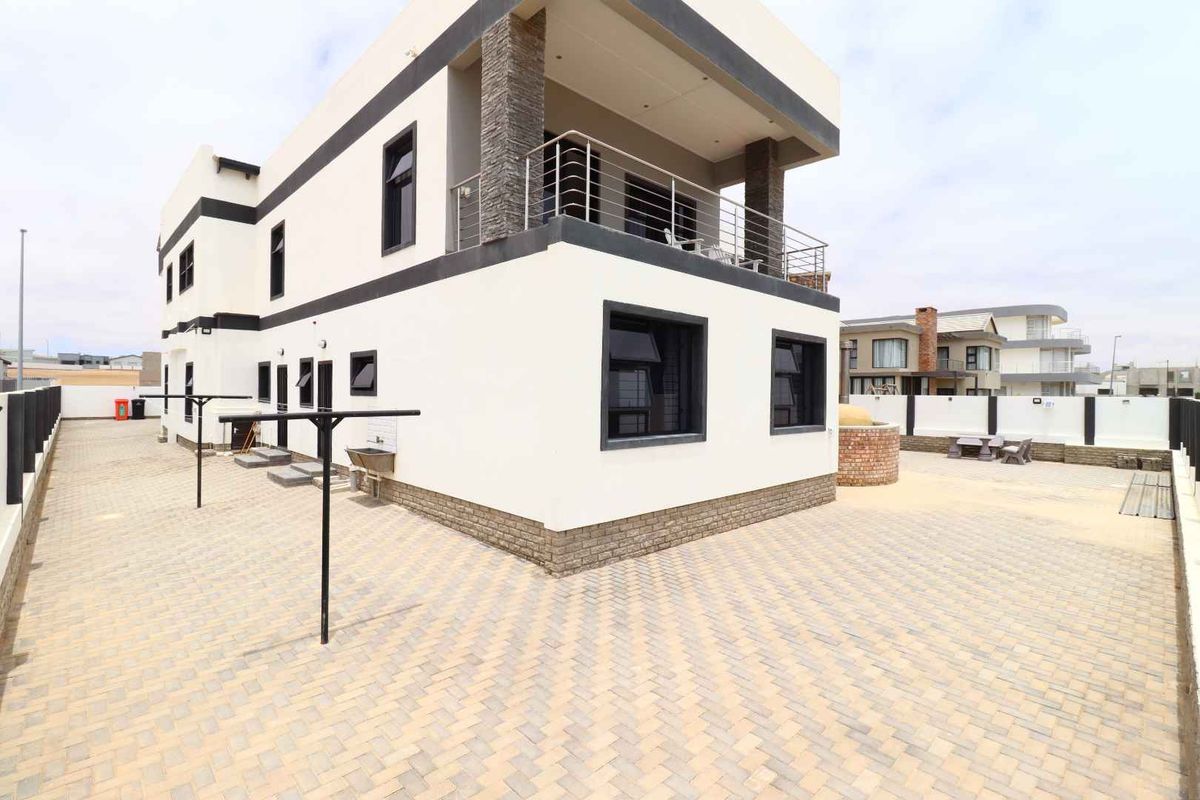 Rear view of a modern two-story house featuring a paved courtyard, balcony with stainless steel railing, and stone-clad architectural accents.