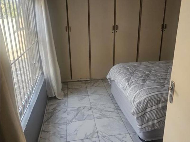 A bedroom featuring built-in cupboards, marble-look tiled flooring, and security bars on the window.
