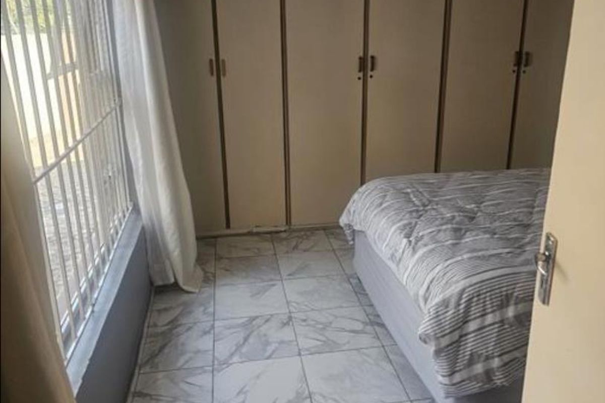 A bedroom featuring built-in cupboards, marble-look tiled flooring, and security bars on the window.