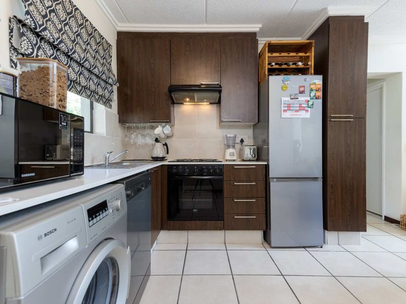 A functional kitchen featuring dark wood cabinetry, tiled flooring, built-in oven with extractor fan, and a tiled backsplash.