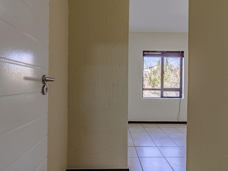 An empty bedroom featuring tiled flooring and a window, viewed from an adjacent hallway through an open doorway.