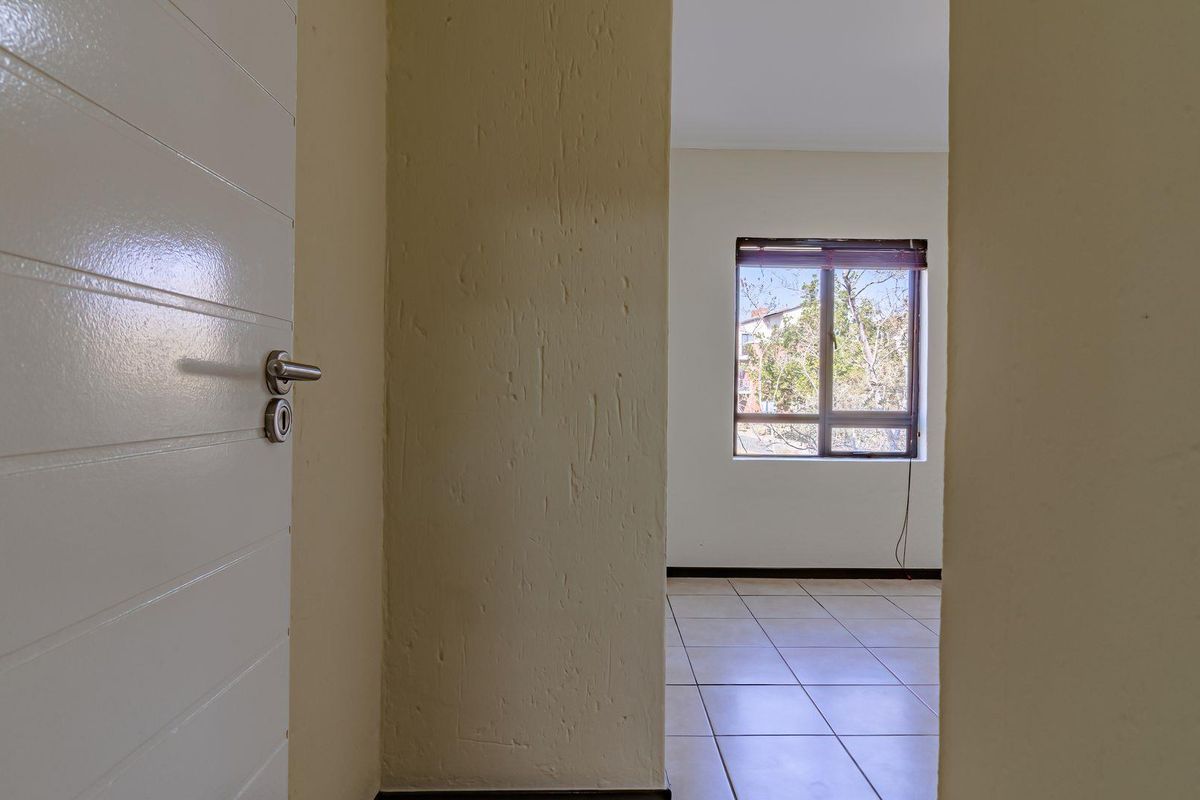 An empty bedroom featuring tiled flooring and a window, viewed from an adjacent hallway through an open doorway.
