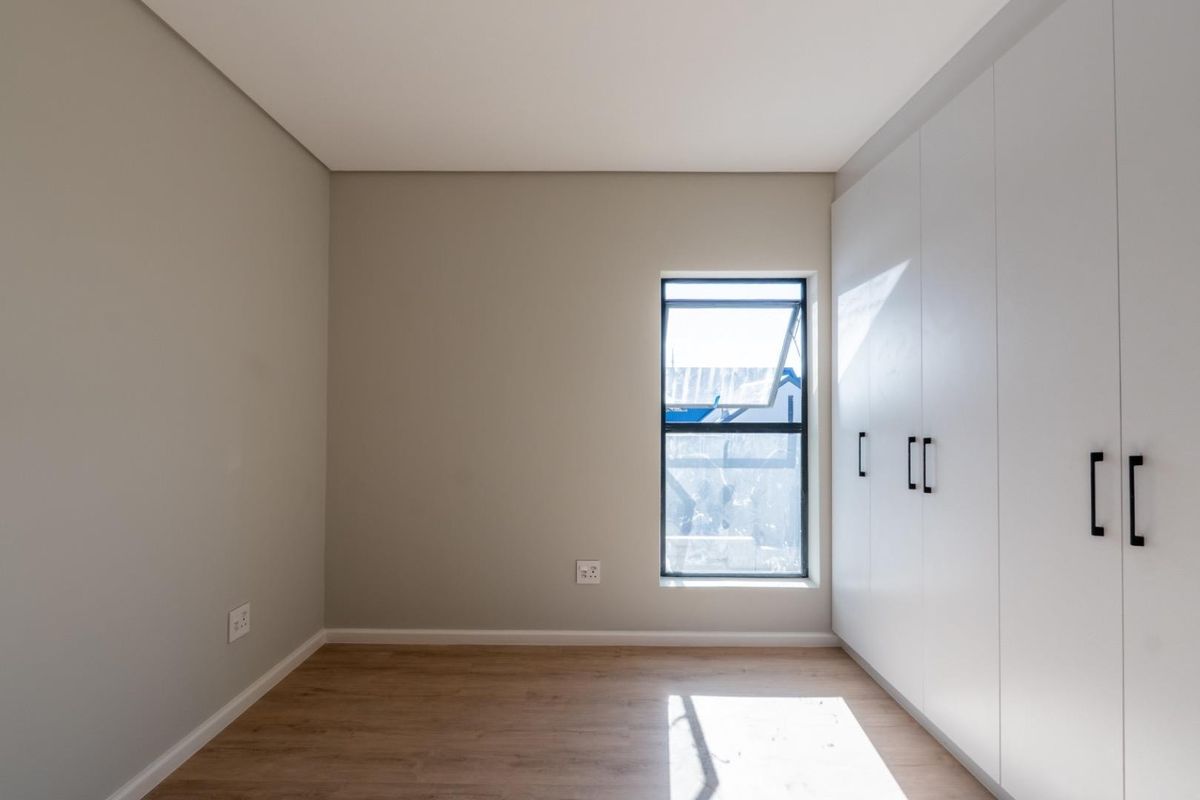 A bright, modern bedroom featuring neutral walls, light wood-look flooring, and floor-to-ceiling built-in wardrobes with sleek black handles.