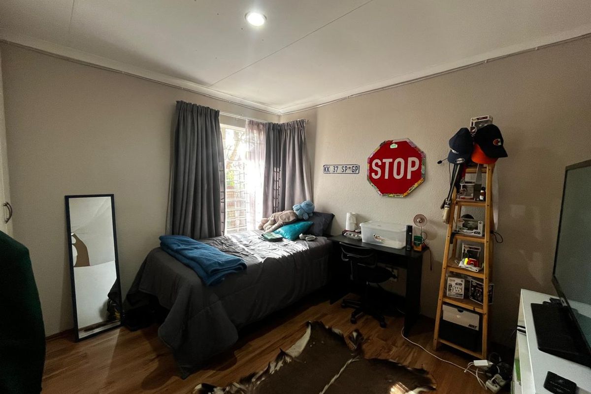 A functional bedroom featuring laminate wood flooring, neutral wall tones, and a window with curtain treatments.