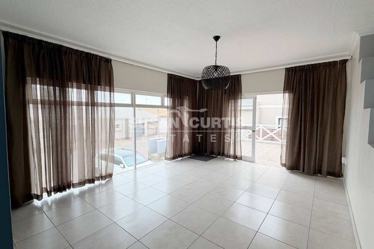 Spacious living area featuring neutral tiled flooring, large glass sliding doors providing natural light, and access to an outdoor patio area.