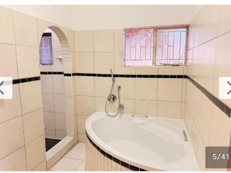 A functional bathroom featuring a corner bathtub, a separate walk-in shower, and neutral ceramic wall tiling with decorative accents.