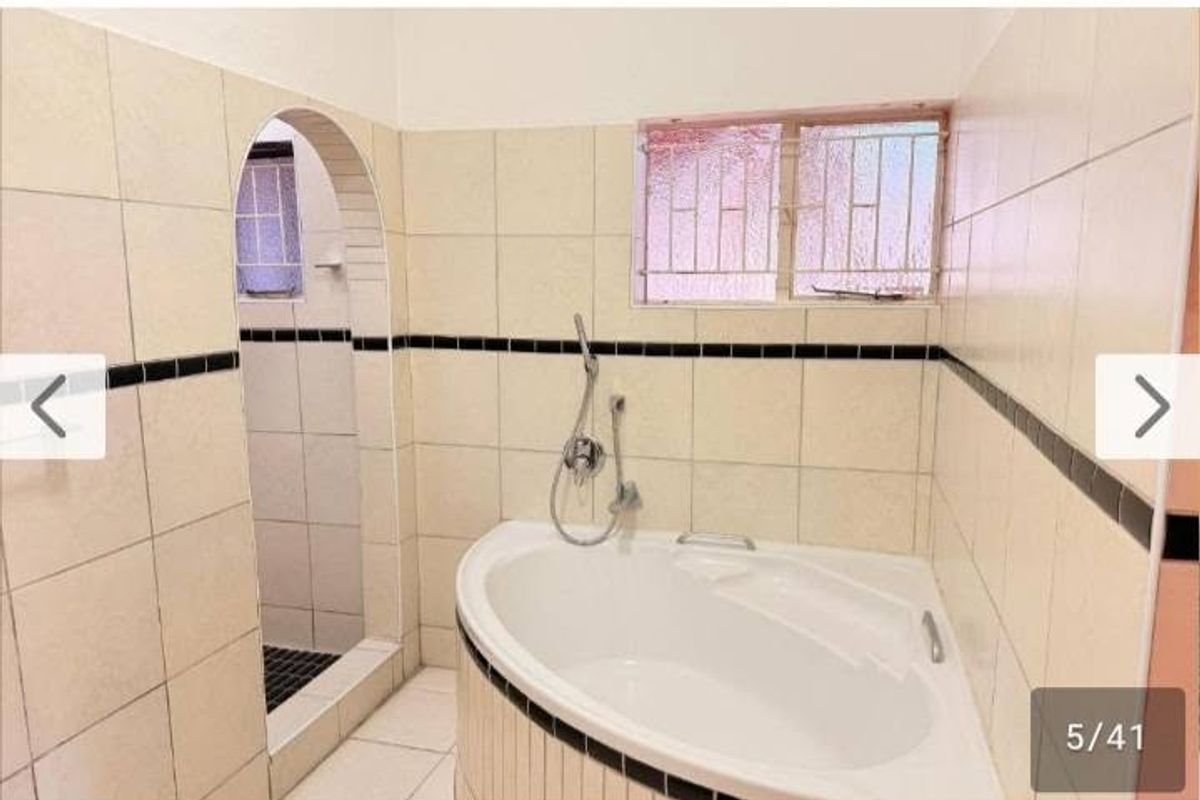 A functional bathroom featuring a corner bathtub, a separate walk-in shower, and neutral ceramic wall tiling with decorative accents.