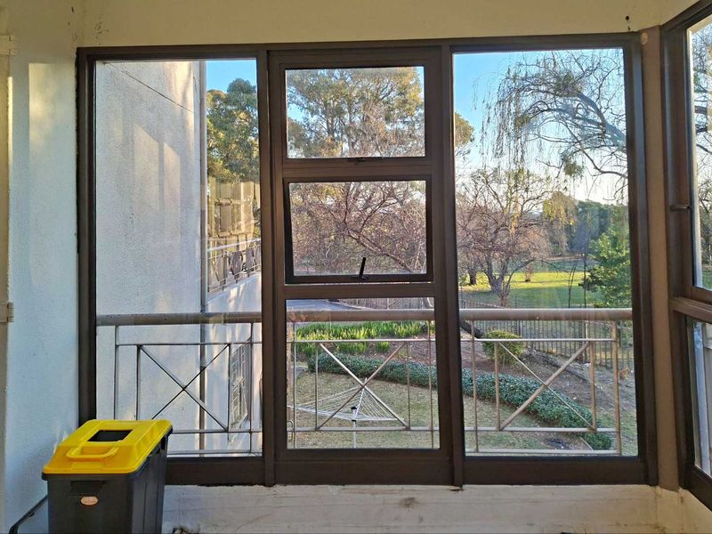 An enclosed balcony area featuring metal balustrades and large aluminium-framed windows overlooking a garden setting.