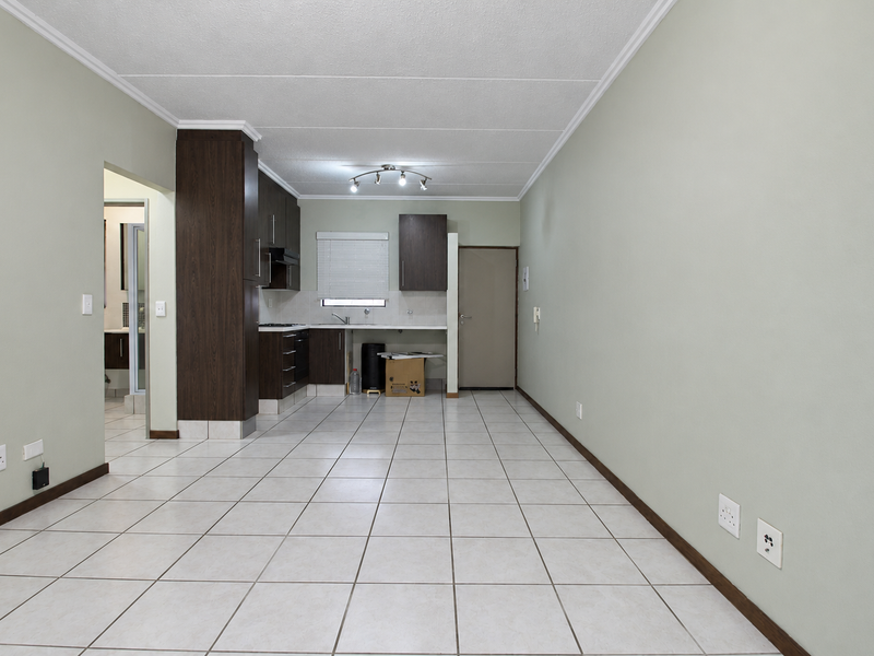 An open-plan living and kitchen area featuring tiled flooring, dark wood cabinetry, and neutral wall tones, providing a clean and functional space.