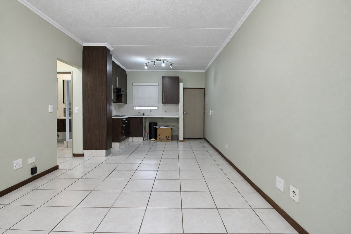 An open-plan living and kitchen area featuring tiled flooring, dark wood cabinetry, and neutral wall tones, providing a clean and functional space.