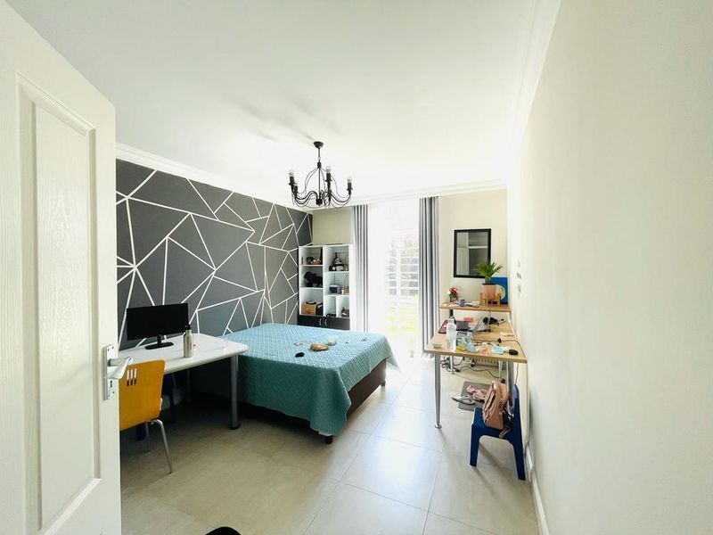 A well-lit bedroom featuring tiled flooring, a decorative feature wall, and a sliding glass door providing access to natural light.