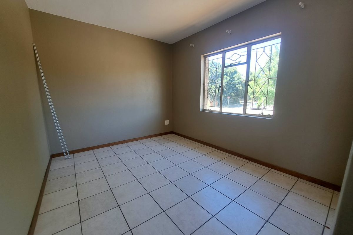 An empty bedroom featuring neutral wall paint, tiled flooring, and a window fitted with security bars.