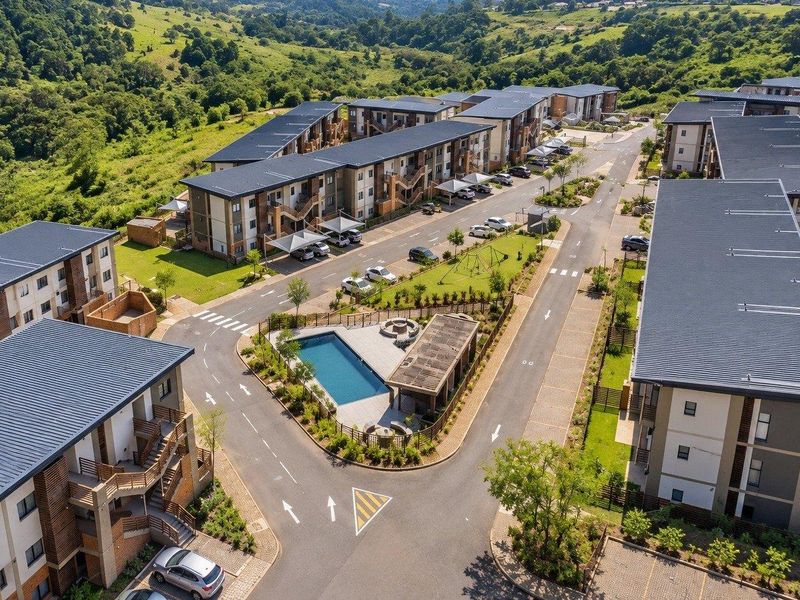 Aerial view of a modern apartment complex featuring communal swimming pool, clubhouse, landscaped grounds, and dedicated covered parking areas.