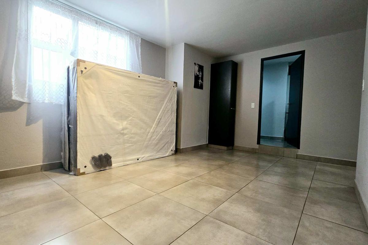 A neutral bedroom featuring large format floor tiles and a built-in storage cupboard, offering a clean and versatile space ready for personalization.