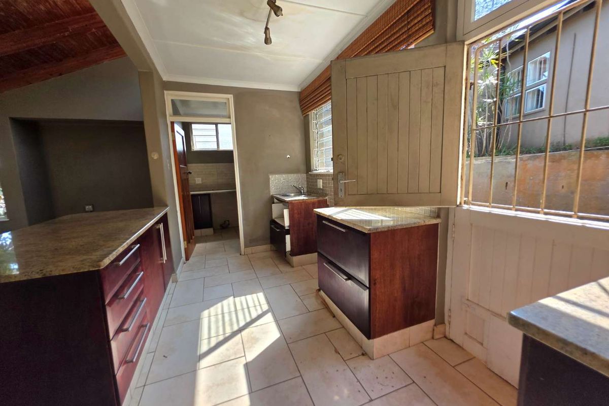 A functional kitchen area featuring dark wood cabinetry, granite countertops, tiled flooring, and a stable-style door leading to the exterior.