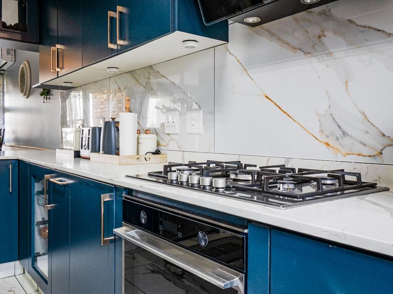 Modern kitchen featuring deep blue cabinetry, stone countertops, a marble-look splashback, and integrated gas hob with oven.