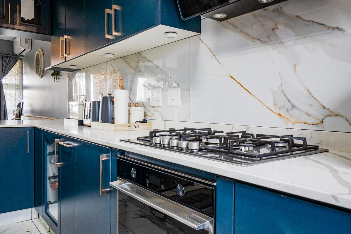 Modern kitchen featuring deep blue cabinetry, stone countertops, a marble-look splashback, and integrated gas hob with oven.