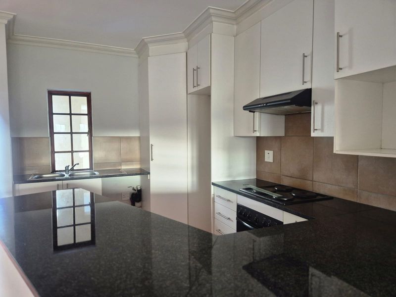 Modern kitchen featuring granite countertops, ample built-in cabinetry, integrated electric hob and oven, extractor fan, and a double sink with tiled backsplash.