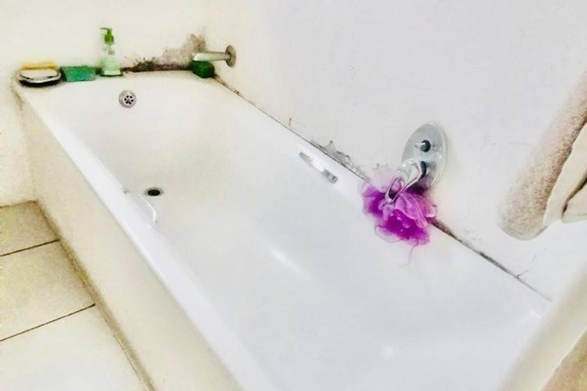 A bathroom featuring a built-in bathtub with chrome fixtures, requiring maintenance due to visible wall staining and damaged sealant around the tub area.