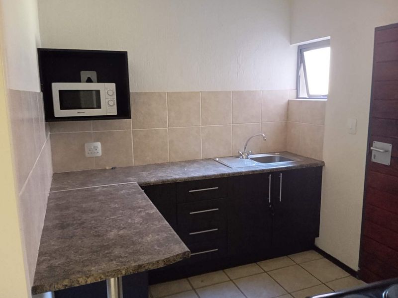 A functional scullery or secondary kitchen area featuring dark cabinetry, laminate countertops, a stainless steel sink, and tiled backsplash.