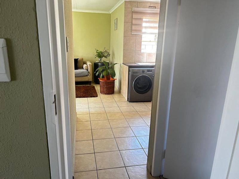 An open-plan living and kitchen area featuring tiled flooring, built-in cabinetry, and a functional laundry setup with a washing machine.