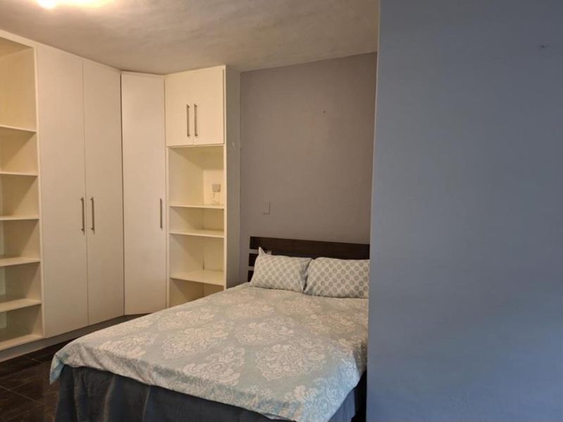 A bedroom featuring extensive built-in cabinetry with integrated shelving and wardrobes, finished with dark tiled flooring.
