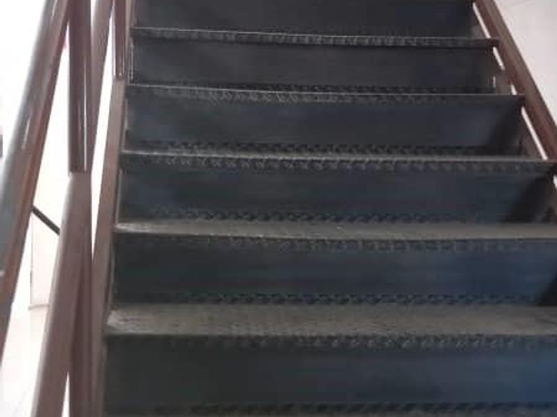Industrial metal staircase with handrails providing access to an upper level, featuring durable tread plates and tiled flooring at the base.