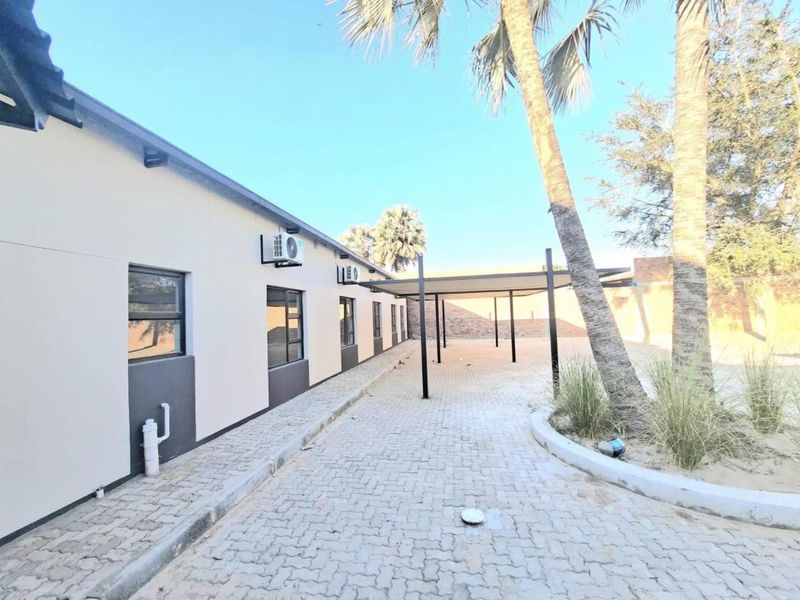 Rear exterior view of the office building featuring a paved driveway, covered carport parking, and wall-mounted air conditioning units.
