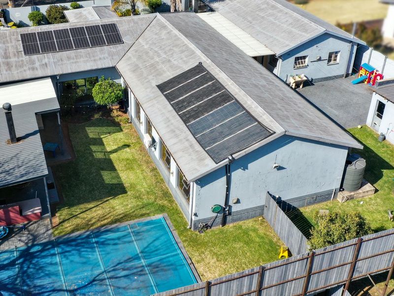Aerial view of the property featuring a corrugated metal roof with solar installations, a swimming pool with cover, and a private garden area.