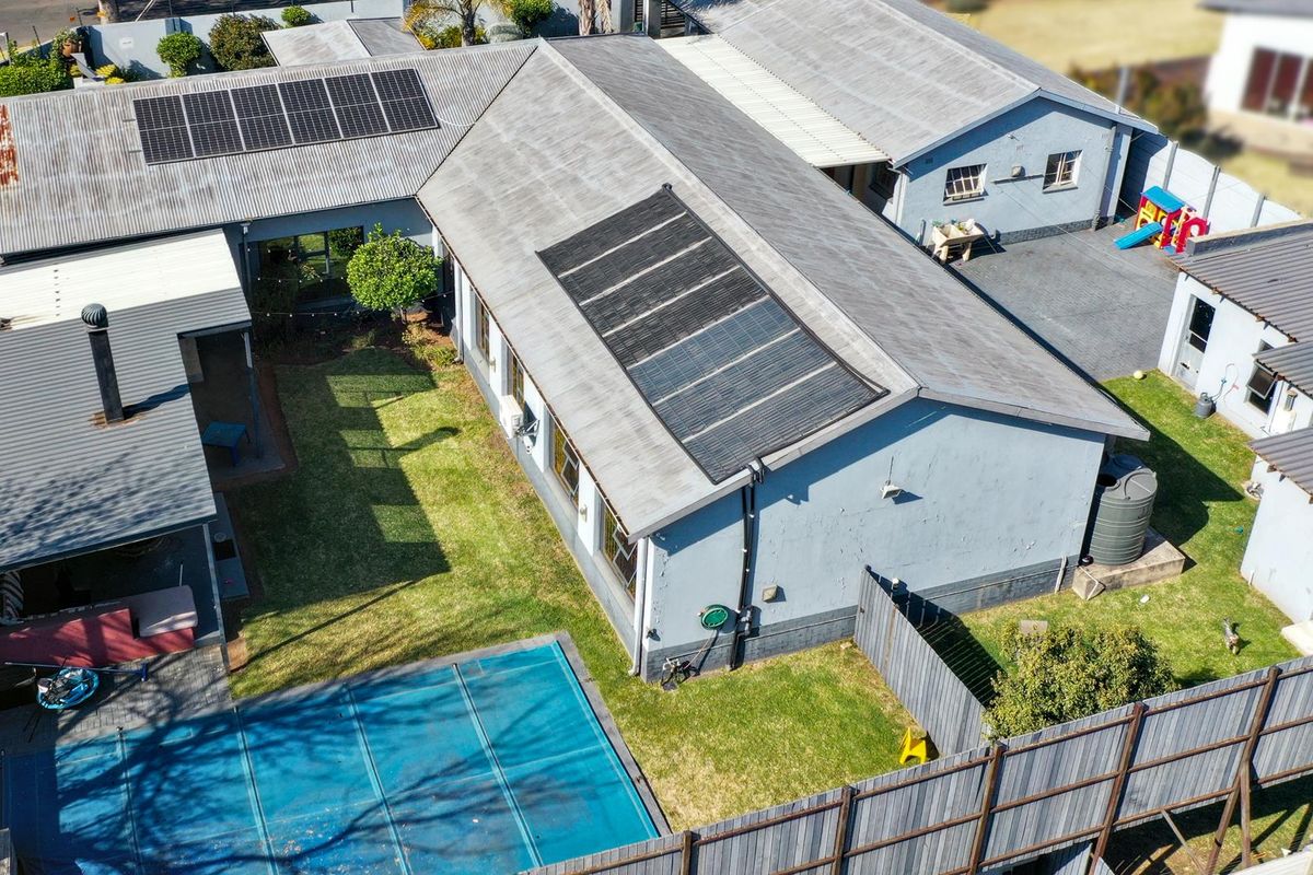 Aerial view of the property featuring a corrugated metal roof with solar installations, a swimming pool with cover, and a private garden area.