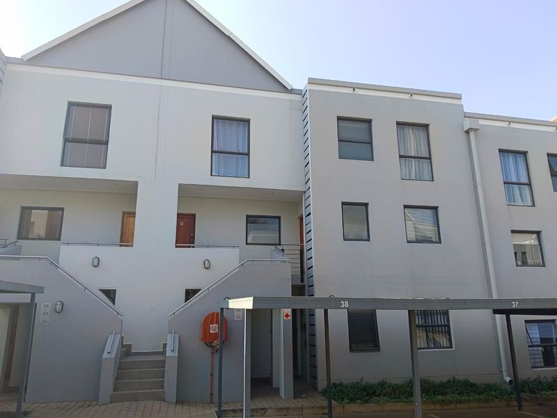 Front elevation of a multi-story apartment complex featuring modern grey facade, external staircases, and covered carport parking bays.