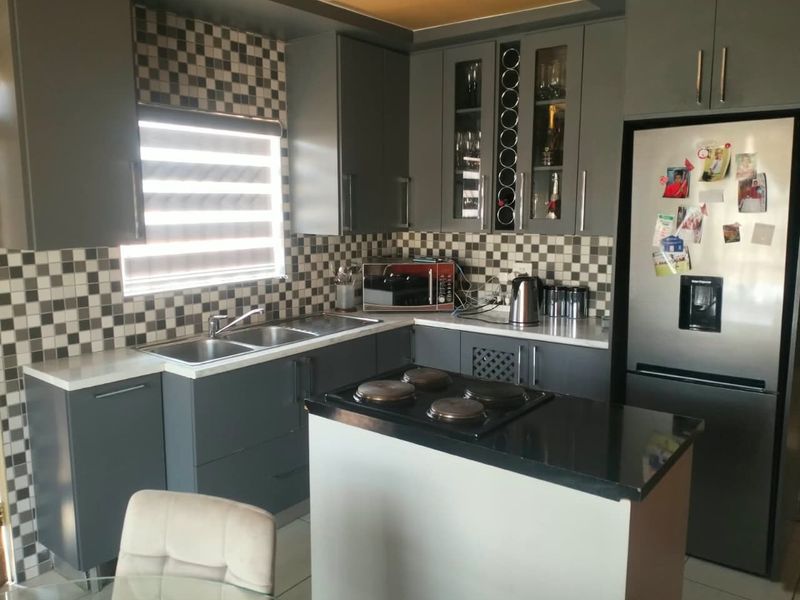 Modern kitchen featuring dark grey cabinetry, stone countertops, a tiled backsplash, and a central island with a built-in hob.