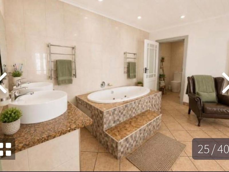 Spacious bathroom featuring a double vanity with granite countertops, a raised built-in bathtub with mosaic tiling, and heated towel rails.