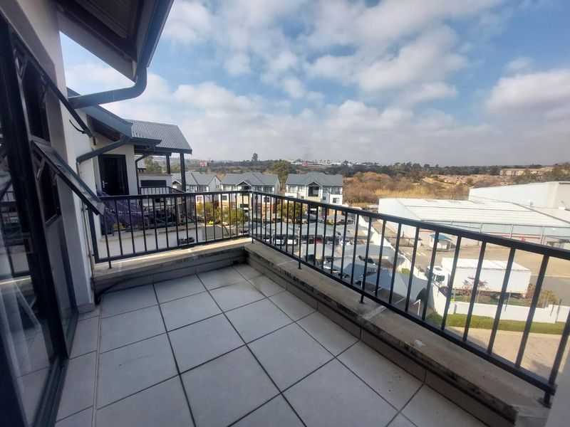 A spacious balcony featuring tiled flooring and a metal balustrade, offering an elevated view of the surrounding complex and landscape.