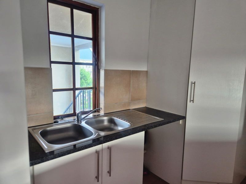 A functional kitchen area featuring a double bowl stainless steel sink, dark laminate countertops, tiled splashback, and white built-in cabinetry.
