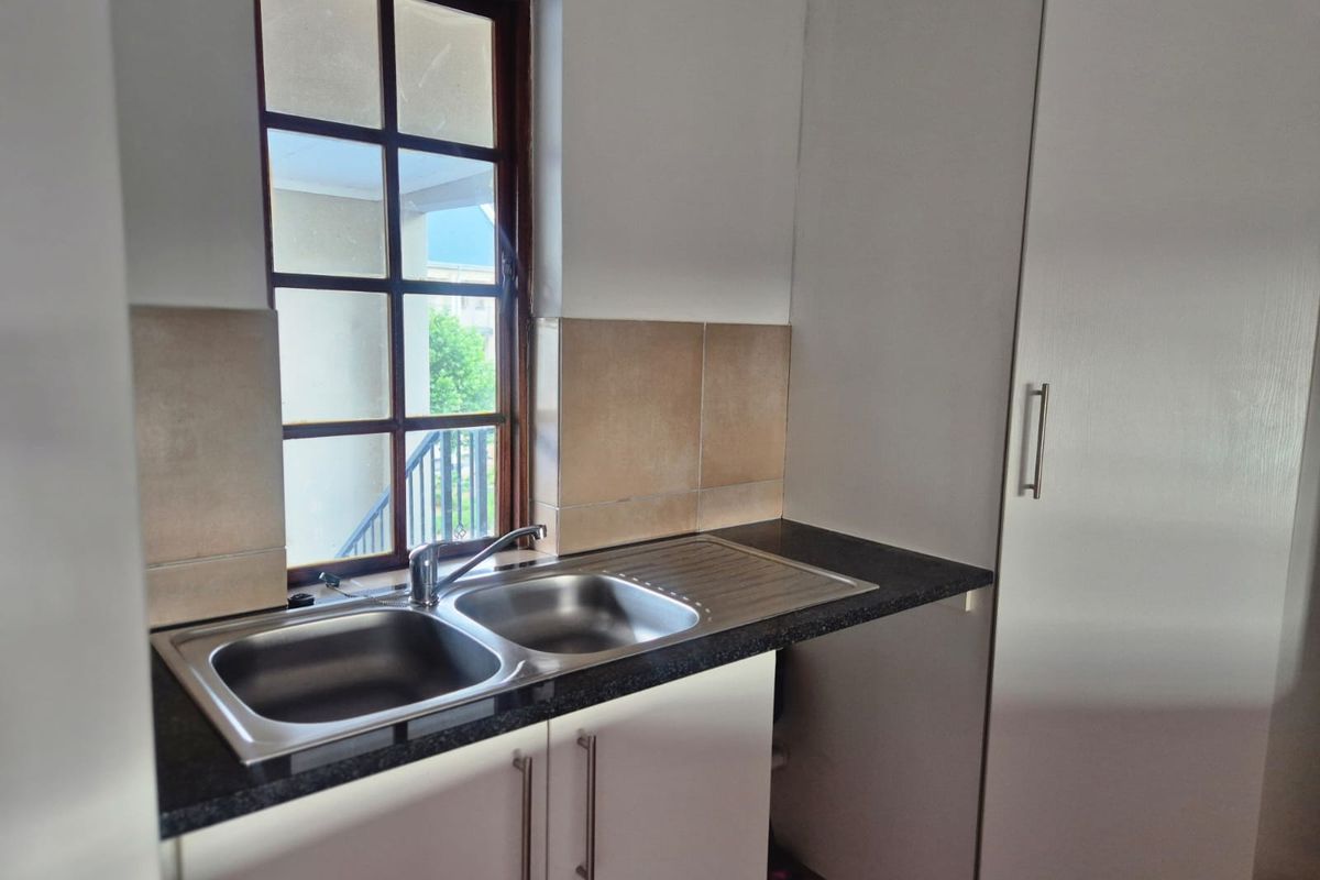 A functional kitchen area featuring a double bowl stainless steel sink, dark laminate countertops, tiled splashback, and white built-in cabinetry.