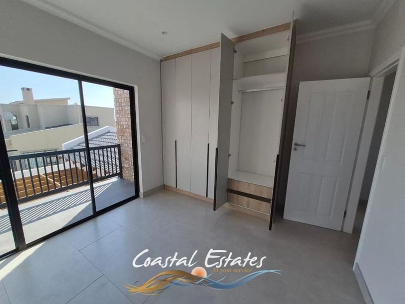 Bright bedroom featuring modern built-in cupboards, neutral tiled flooring, and a large sliding glass door providing access to an outdoor balcony.