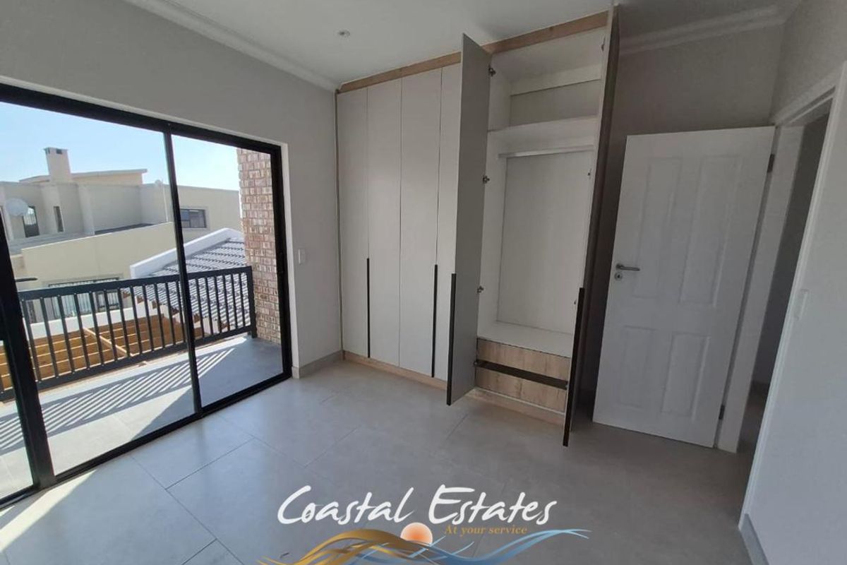 Bright bedroom featuring modern built-in cupboards, neutral tiled flooring, and a large sliding glass door providing access to an outdoor balcony.