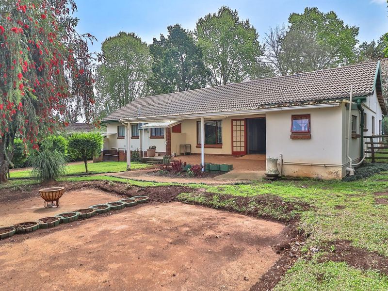 Rear view of the house featuring a covered patio area, tiled roof, and a large garden space with established trees.