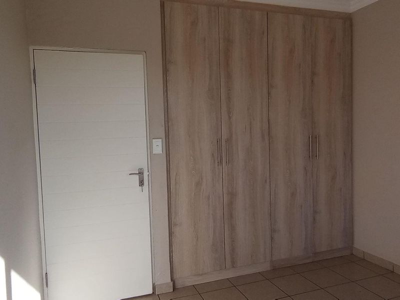 A clean, empty bedroom featuring neutral tiled flooring and modern wood-finish built-in cupboards.