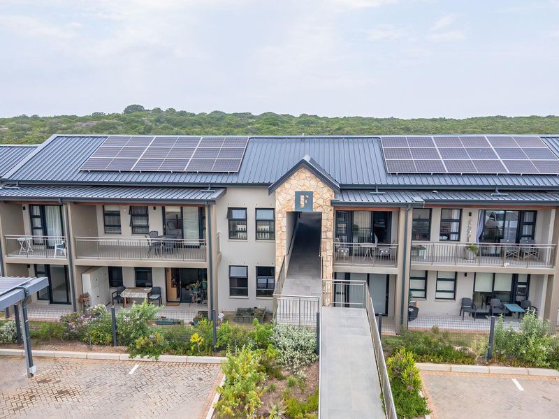 Aerial view of a modern retirement village building featuring solar panels, stone accents, and private balconies overlooking a landscaped parking area.