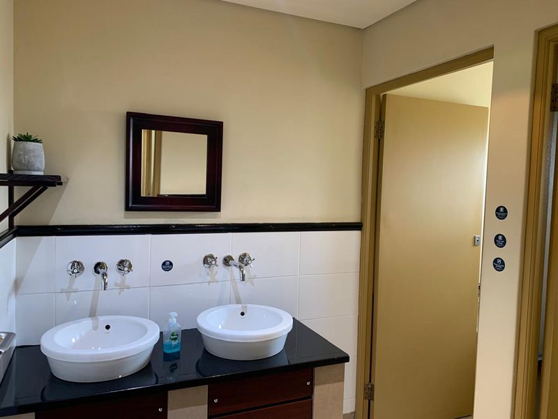 A functional office bathroom featuring a double vanity with vessel sinks, chrome fixtures, and a tiled splashback.