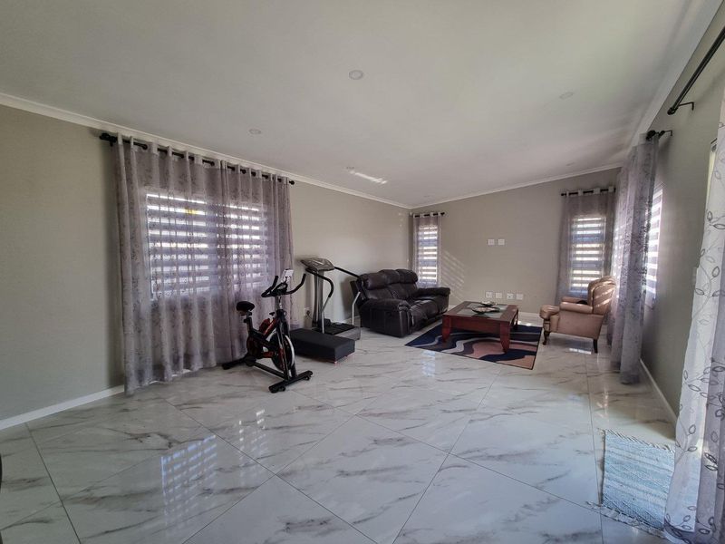 Spacious living area featuring polished marble-look porcelain floor tiles, recessed downlighting, and neutral wall finishes, offering a bright and versatile open-plan space.