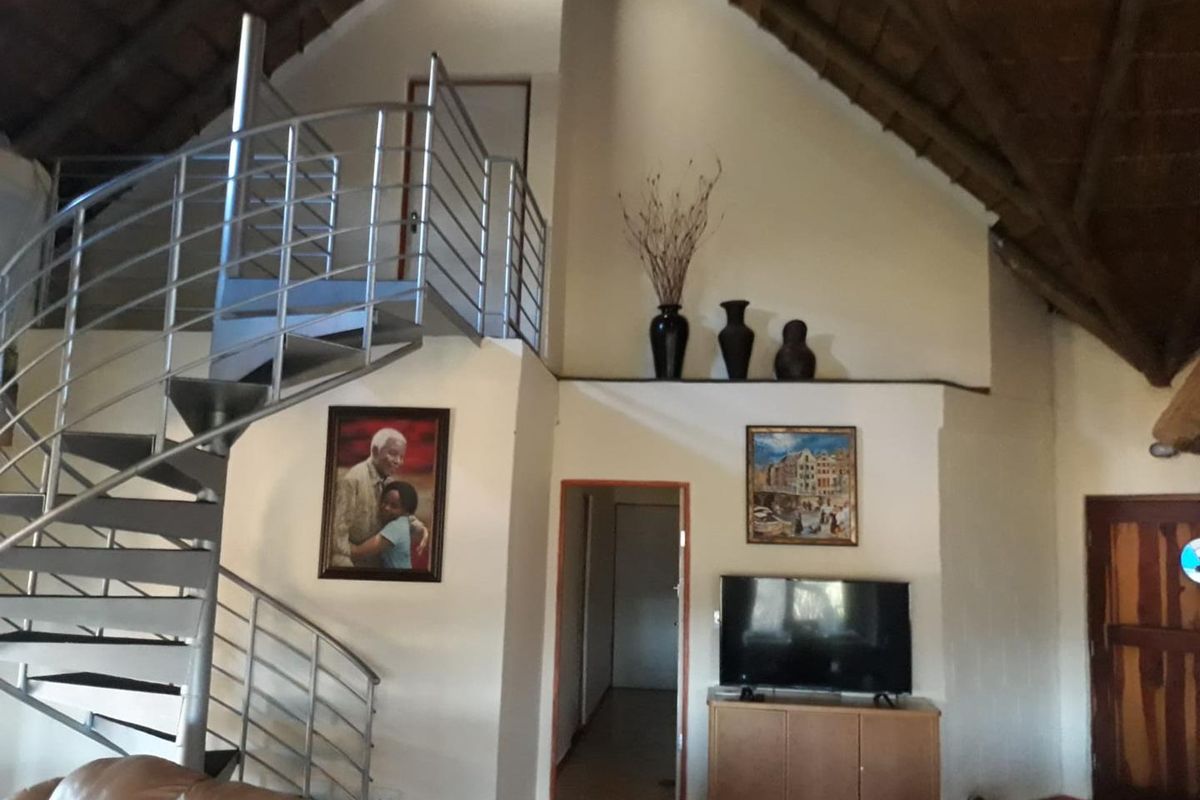 A spacious living area featuring a high vaulted ceiling, exposed timber beams, and a modern metal spiral staircase leading to an upper level.