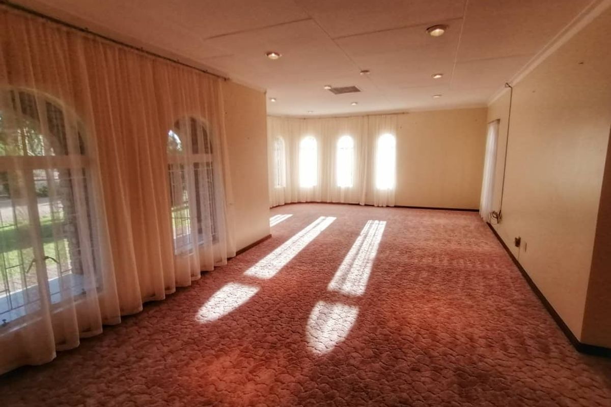 A spacious, empty living area featuring large arched windows, recessed lighting, and wall-to-wall carpeting, offering a blank canvas for renovation.