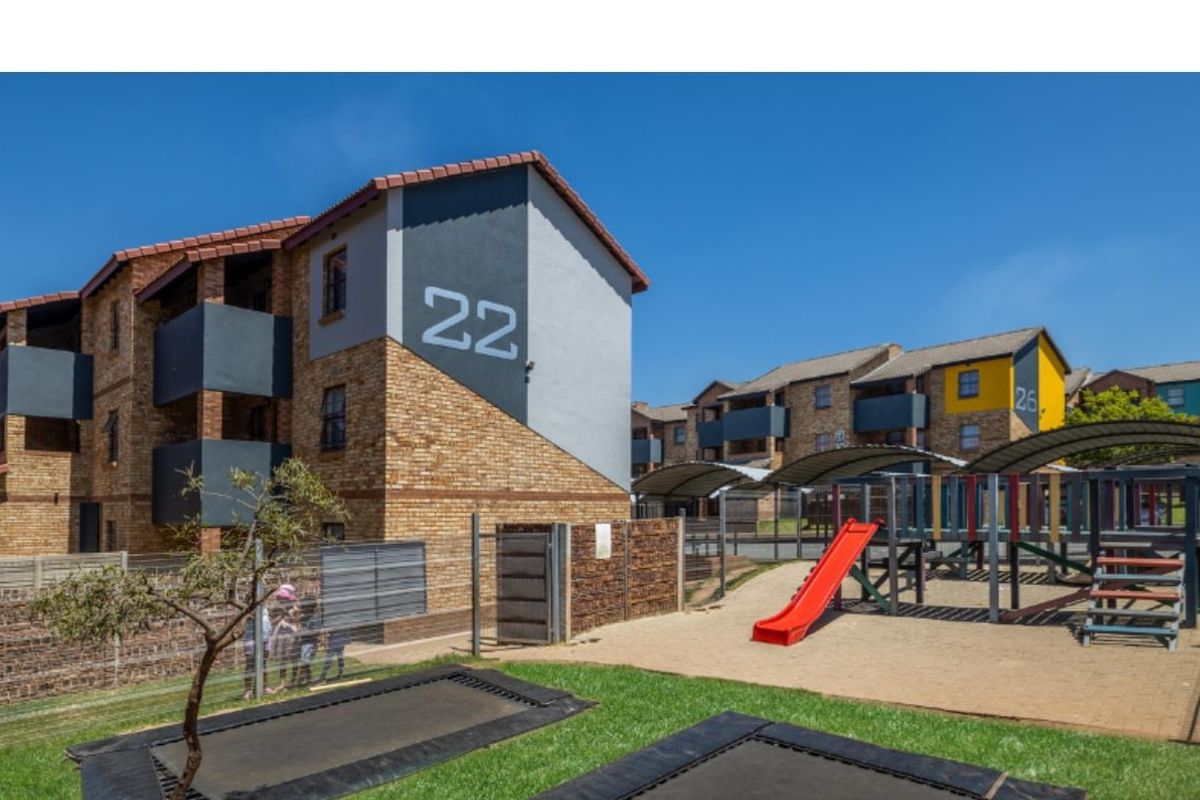 Exterior view of a multi-story apartment complex featuring brick and painted facades, with an adjacent communal playground and recreational area.